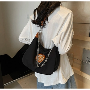 Detail of black half-moon bag with metallic M logo, silver chain and leather strap