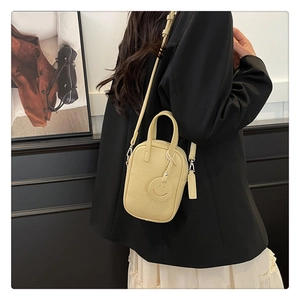 Detail view of pale yellow pebble leather mini square bag with a cute smiley face charm