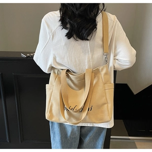 Detail of beige canvas tote bag showing wide adjustable strap and script lettering design
