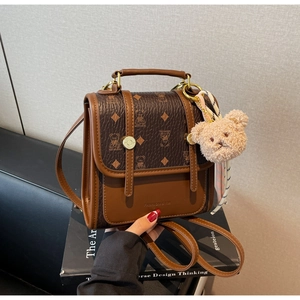 Detail view of brown vintage handbag featuring bear pattern, plush charm, and silk scarf