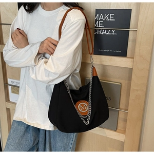 Detail of black nylon shoulder bag with orange logo patch and silver chain strap
