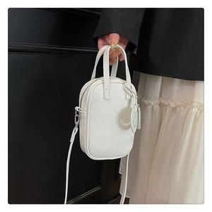 Close-up of white lychee leather square handbag with top zipper and round charm detail