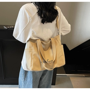 Detail of canvas tote bag with artistic lettering, side pockets, and adjustable strap