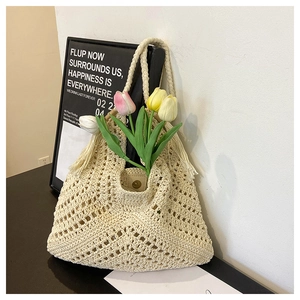 Detail of hand-woven beige straw tote bag featuring bohemian tassels and texture