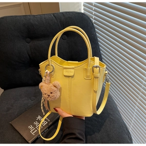 Detail of yellow bucket bag with Chris 2ab logo and brown teddy bear charm accessory