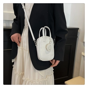 Close-up of white lychee leather mini crossbody bag with smiley charm and top handles