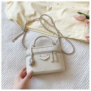 Detail der cremeweißen Mini-Box-Tasche aus Leder mit Herzanhänger und Metallkette