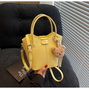 Detail of yellow bucket bag with smooth PU leather, logo embossing and teddy bear charm