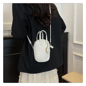 White litchi pattern mini tote bag shown on black suit with crossbody strap detail