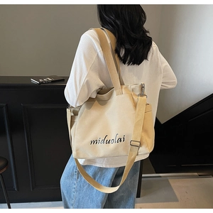 Close-up of beige canvas tote bag featuring adjustable shoulder strap and side pocket detail