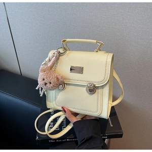 Close-up of creamy yellow PU leather backpack with metal buckles and plush bear charm