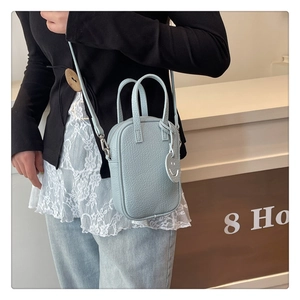 Close-up of light blue pebble leather crossbody bag with cute charm on a female model