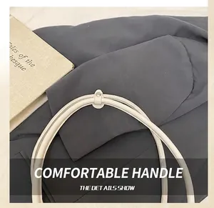 Detailed close-up of smooth cream-colored tote bag handles with silver metal rivets