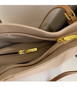 Détail des doubles fermetures éclair dorées avec logo SOU KU gravé sur un sac en cuir beige