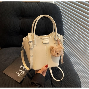 Detail of off-white bucket bag with plush bear charm and striped scarf decoration