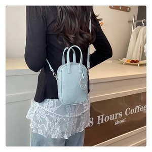 Close-up of light blue pebble leather crossbody bag with minimalist smiley face charm
