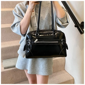Detail of black patent leather Boston bag with silver zipper and glossy finish shown on model