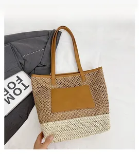 Close-up of contrast color woven straw tote bag with brown leather straps on white fabric
