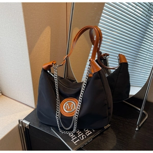 Detailed shot of half-moon black canvas bag with leather M logo and chain strap
