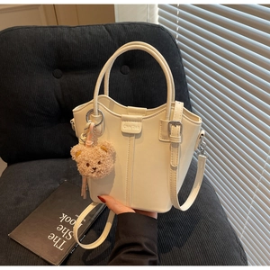 Detailed shot of white PU leather bucket bag with silver hardware and brown teddy bear charm