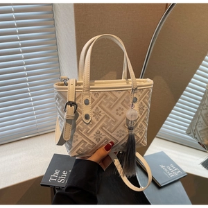 Detail of mini cream tote bag featuring floral embroidery and grey tassel charm
