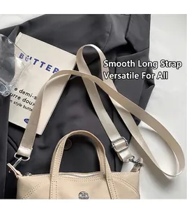 Detail of cream canvas crossbody bag with silver metal logo and smooth shoulder strap