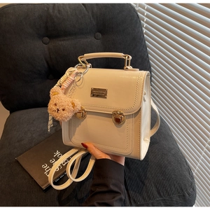 Close-up of beige PU leather backpack with gold metal clasp and brown teddy bear charm