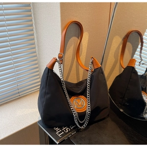 Detail of black nylon crossbody bag with brown leather strap and silver chain accent