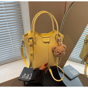 Detail of yellow bucket bag with Chrs'2ab embossed logo and cute plush bear charm