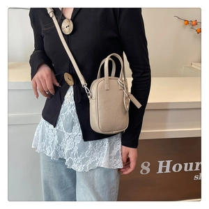 Close-up of beige square crossbody bag with pebble leather texture and side charm