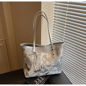 Detail der silbernen Metallic-Tasche mit weißer Spitzenschleife und Perlenquasten