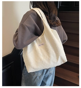 Close-up of white tote bag featuring 3D dot texture fabric and light purple woven label