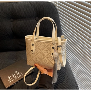 Detail of a mini cream bucket bag featuring floral jacquard patterns and a grey tassel