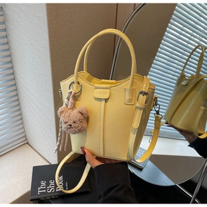 Detail of light yellow bucket bag with glossy PU finish and a brown teddy bear charm