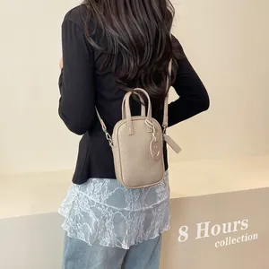 Model view of beige pebble grain mini crossbody bag with smiley charm and dual handles