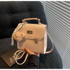 Detail of a beige structured handbag with gold hardware, bear charm, and striped ribbon