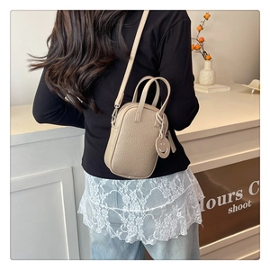 Rear view of a beige pebble leather mini crossbody bag with a round smiley face charm