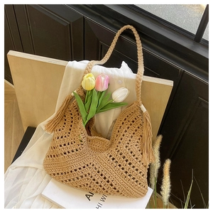 Detail of hand-woven straw tote bag featuring bohemian tassels and hollow diamond texture