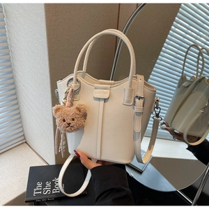 Detail of white leather bucket bag featuring silver hardware and a brown bear charm