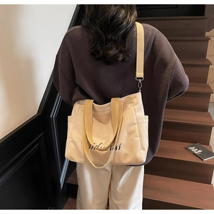 Canvas tote bag with yellow straps shown on model's shoulder near wooden stairs