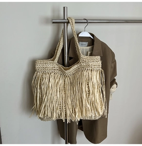 Détail d'un sac cabas en paille beige avec des franges en raphia et une large poignée tissée