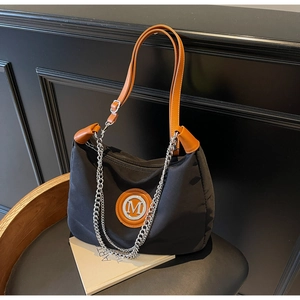 Detail of black nylon tote bag featuring tan leather straps and metal M logo