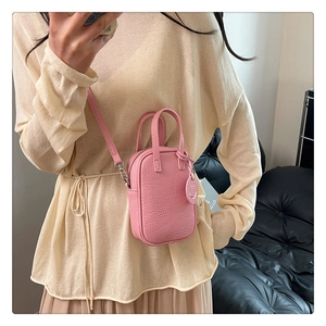 Pink lychee grain leather mini handbag with a smiley charm shown in a mirror selfie
