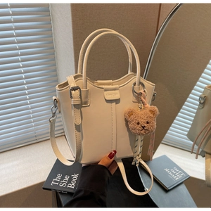 Detailed shot of white PU leather bucket bag with teddy bear charm and logo tag