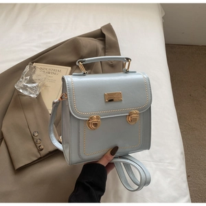 Detail of light blue faux leather handbag with gold locks and beige topstitching