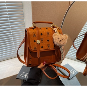 Close-up of brown textured leather backpack featuring bear print and plush charm detail