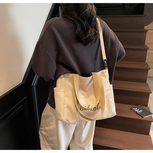 Detail of canvas tote bag with khaki straps and side pockets on wooden stairs