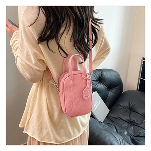 Detail view of pink lychee grain mini handbag with adjustable strap and smiley charm tag