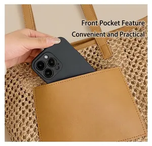 Detail of straw tote bag with brown leather front pocket holding a smartphone