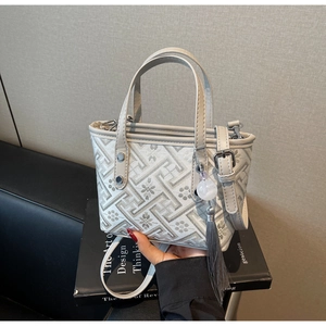 Detail of grey bucket bag with geometric patterns, tassel, and silver hardware on a book